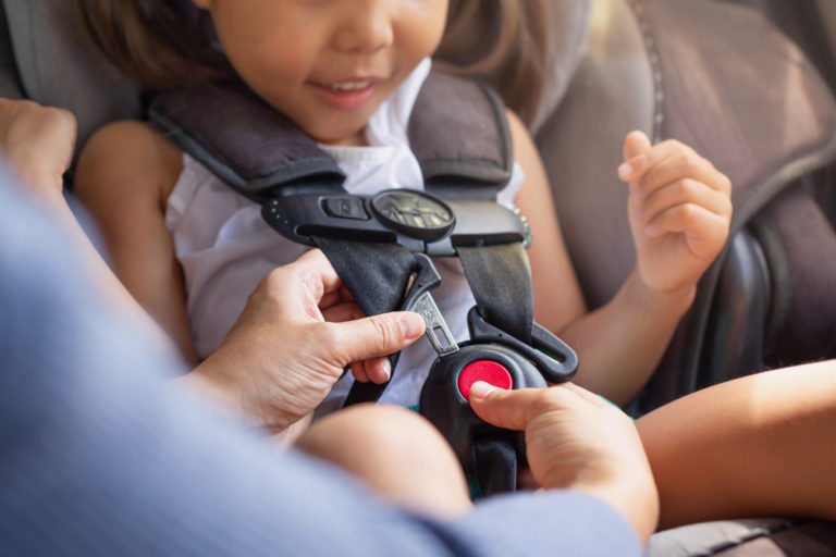 adult clipping child into a car seat