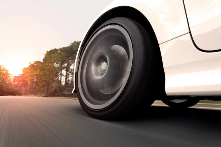 A white car on a road driving fast into the sunset. Close up on the wheel.
